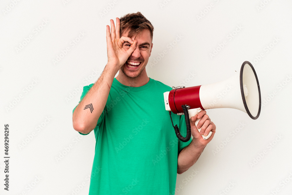 Young caucasian man holding megaphone isolated on white background excited keeping ok gesture on eye. Young caucasian man holding megaphone isolated on white background excited keeping ok gesture on eye.