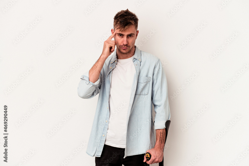Young caucasian man holding crutch isolated on white background pointing temple with finger, thinking, focused on a task. Young caucasian man holding crutch isolated on white background pointing temple with finger, thinking, focused on a task.