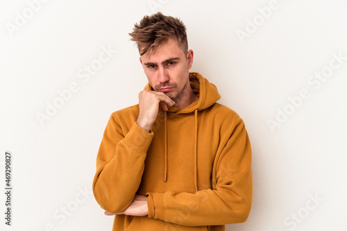 Young caucasian man isolated on white background suspicious, uncertain, examining you.