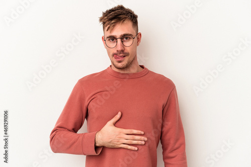 Young caucasian man isolated on white background touches tummy, smiles gently, eating and satisfaction concept.