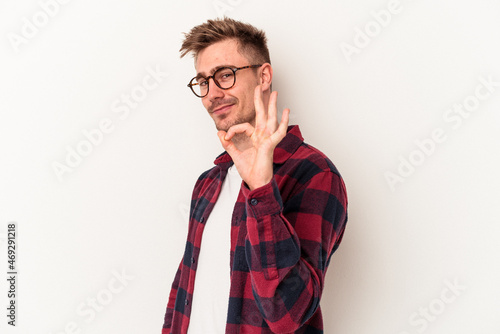 Young caucasian man isolated on white background winks an eye and holds an okay gesture with hand.