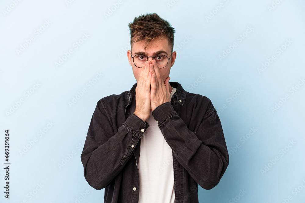 Young caucasian man isolated on blue background shocked, covering mouth with hands, anxious to discover something new. Young caucasian man isolated on blue background shocked, covering mouth with hands, anxious to discover something new.