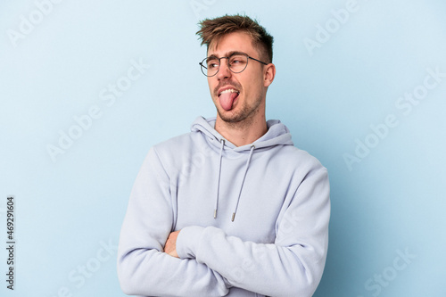 Young caucasian man isolated on blue background funny and friendly sticking out tongue.