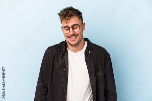 Young caucasian man isolated on blue background laughs and closes eyes, feels relaxed and happy.