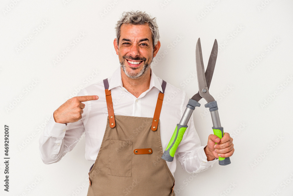 Middle age gardener man holding a scissors isolated on white background person pointing by hand to a shirt copy space, proud and confident Middle age gardener man holding a scissors isolated on white background person pointing by hand to a shirt copy space, proud and confident
