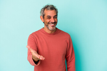 Middle age caucasian man isolated on blue background  stretching hand at camera in greeting gesture.