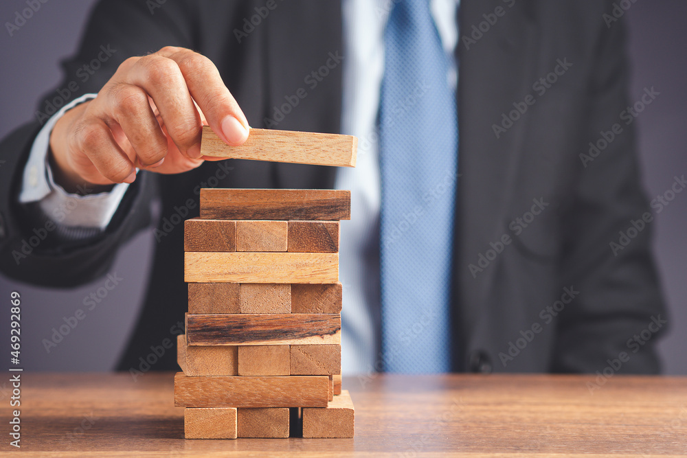 Risk of management and strategy plans for business growth and success concept. Close-up hand of the businessman in a suit playing a wooden block game while sitting at the work table. Space for text Risk of management and strategy plans for business growth and success concept. Close-up hand of the businessman in a suit playing a wooden block game while sitting at the work table. Space for text