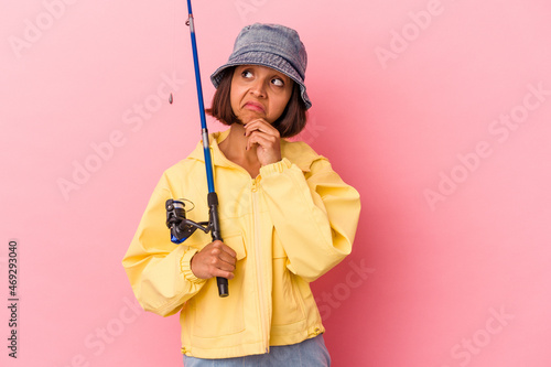 Young mixed race woman practicing fishing isolated on pink background looking sideways with doubtful and skeptical expression. © Asier