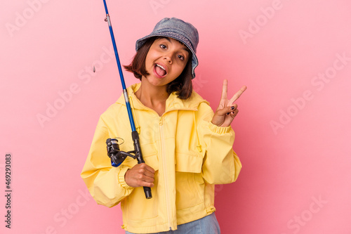Young mixed race woman practicing fishing isolated on pink background joyful and carefree showing a peace symbol with fingers.