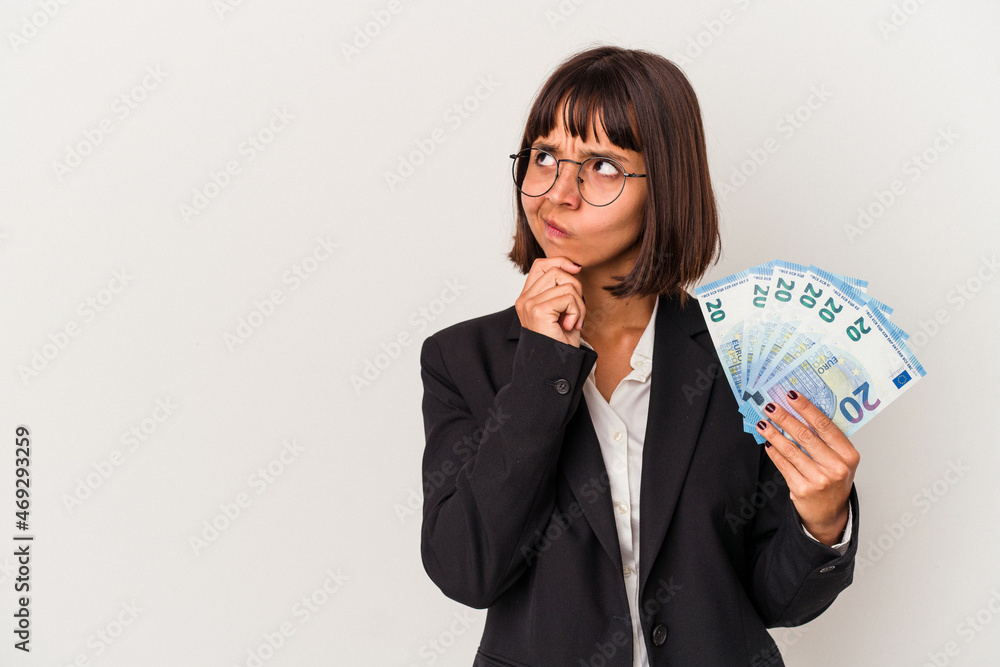 Young mixed race business woman holding a banknotes isolated on white background looking sideways with doubtful and skeptical expression. Young mixed race business woman holding a banknotes isolated on white background looking sideways with doubtful and skeptical expression.