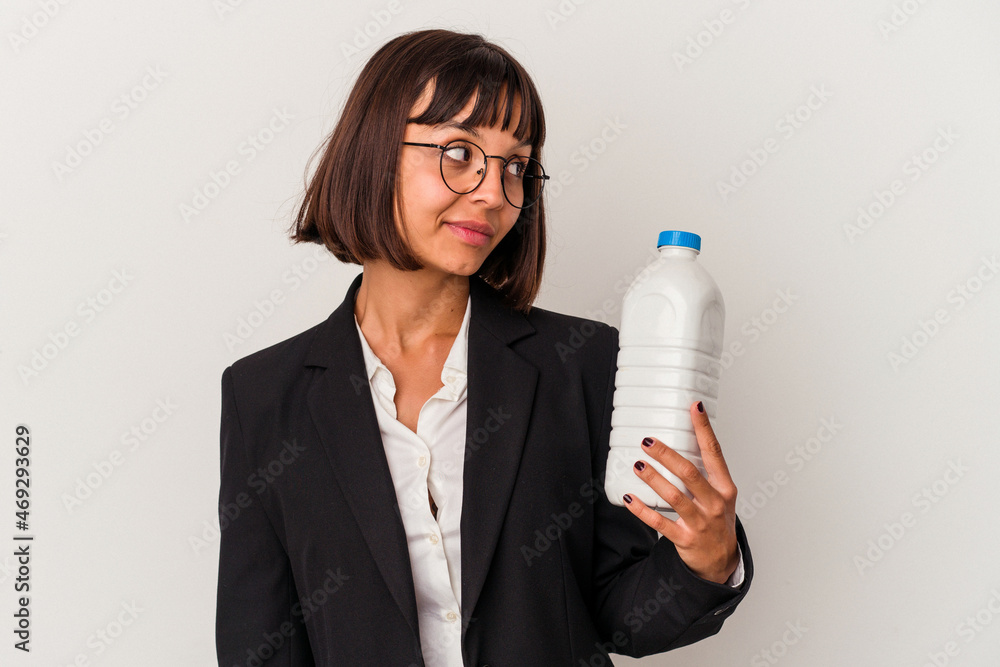 Young mixed race business woman holding a milk bottle isolated on white background looks aside smiling, cheerful and pleasant. Young mixed race business woman holding a milk bottle isolated on white background looks aside smiling, cheerful and pleasant.