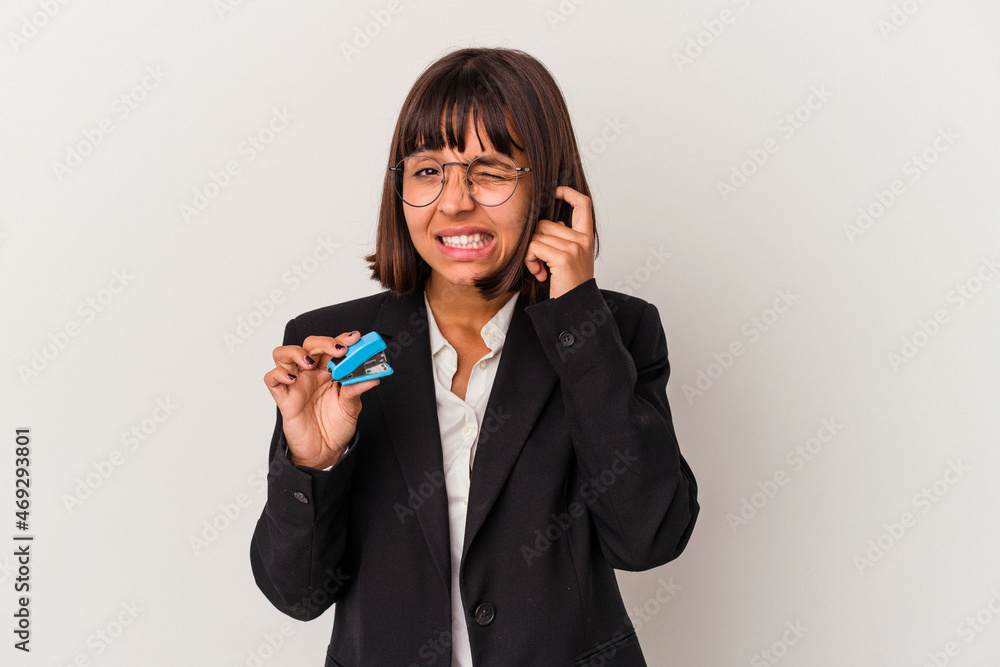 Young mixed race business woman holding a stapler isolated on white background covering ears with hands. Young mixed race business woman holding a stapler isolated on white background covering ears with hands.