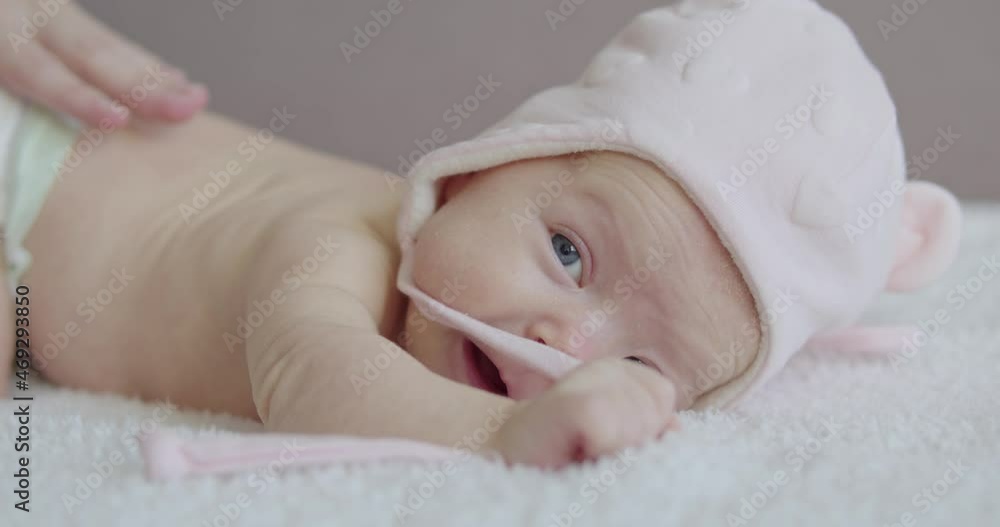 a baby in a diaper lies on his stomach with a hat on his head and mom strokes him on the back a baby in a diaper lies on his stomach with a hat on his head and mom strokes him on the back