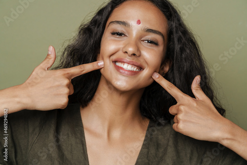 Young south asian woman with bindi pointing fingers at her smile