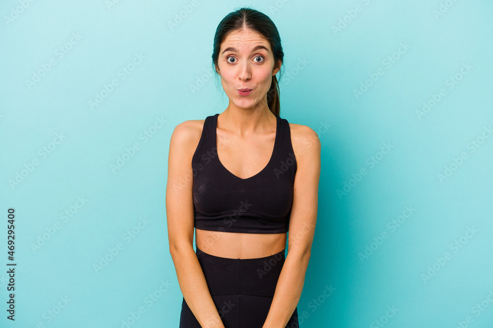 Young sporty caucasian woman isolated on blue background shrugs shoulders and open eyes confused. Young sporty caucasian woman isolated on blue background shrugs shoulders and open eyes confused.