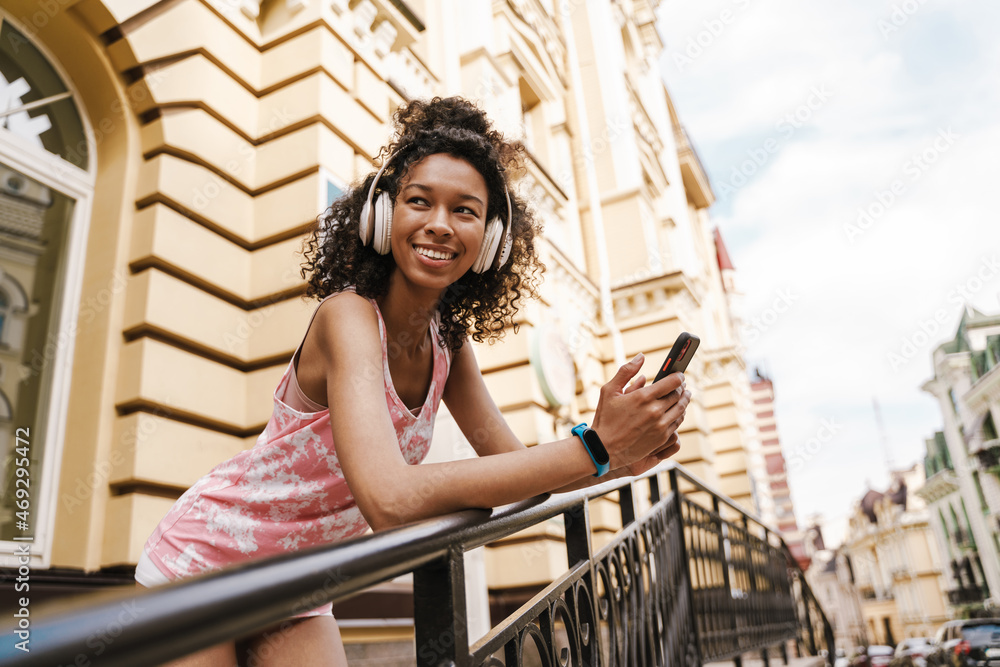 Black woman in headphones smiling while using mobile phone