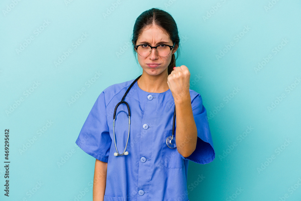 Young caucasian nurse isolated on blue background showing fist to camera, aggressive facial expression. Young caucasian nurse isolated on blue background showing fist to camera, aggressive facial expression.