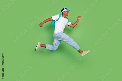 Full size profile photo of funky millennial brunet guy run wear bag t-shirt jeans sneakers isolated on green background