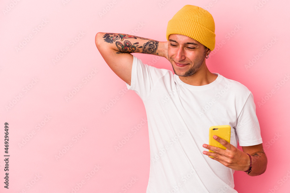 Young caucasian man holding mobile phone isolated on pink background touching back of head, thinking and making a choice. Young caucasian man holding mobile phone isolated on pink background touching back of head, thinking and making a choice.