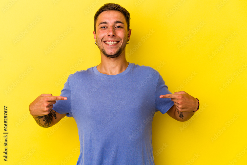 Young caucasian man with tattoos isolated on yellow background points down with fingers, positive feeling. Young caucasian man with tattoos isolated on yellow background points down with fingers, positive feeling.
