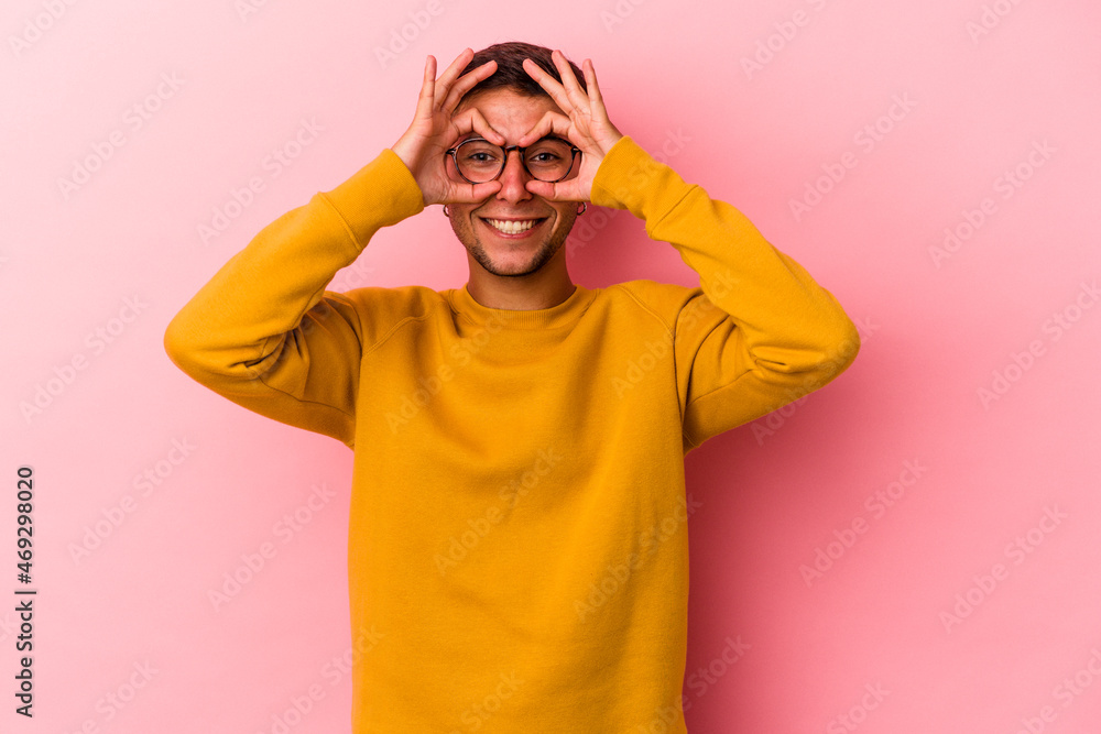 Young caucasian man with tattoos isolated on yellow background showing okay sign over eyes Young caucasian man with tattoos isolated on yellow background showing okay sign over eyes