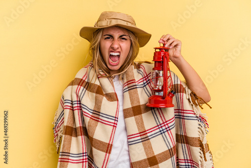 Young caucasian holding lantern isolated on yellow background screaming very angry and aggressive.