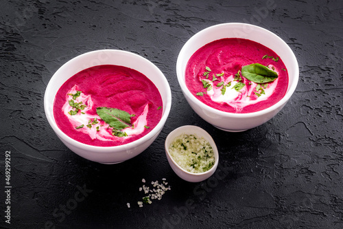 Two white bowls of red beet soup with sour cream and green herbal salt