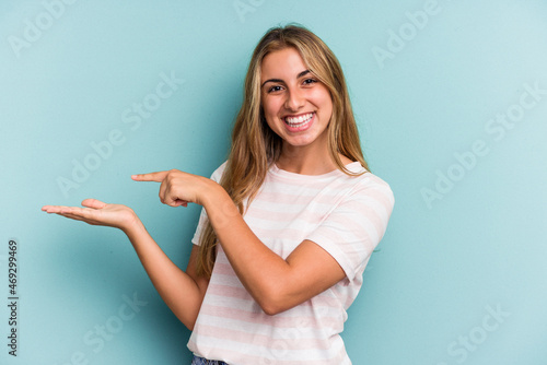 Young caucasian blonde woman isolated on blue background  excited holding a copy space on palm. © Asier