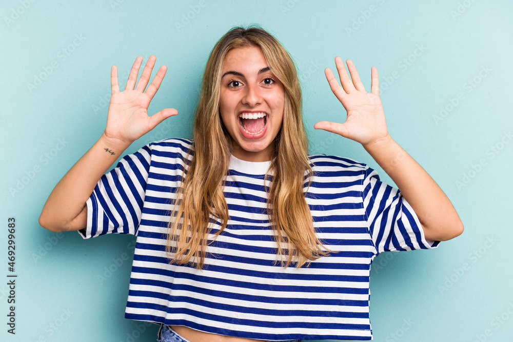 Young caucasian blonde woman isolated on blue background receiving a pleasant surprise, excited and raising hands. Young caucasian blonde woman isolated on blue background receiving a pleasant surprise, excited and raising hands.