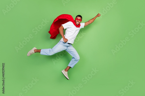 Full length profile photo of impressed super man brunet guy fly wear courage mask t-shirt jeans footwear isolated on green background © deagreez