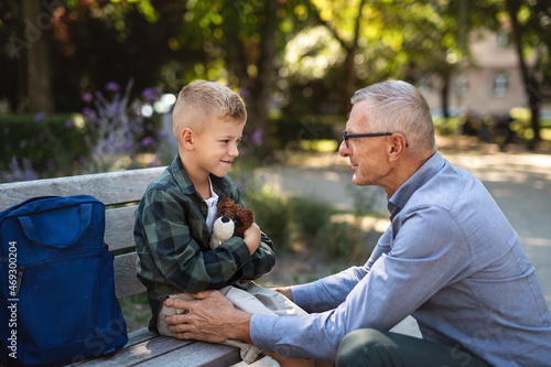 Senior man squatting and talking to grandson outdoors on bench in park. © Halfpoint