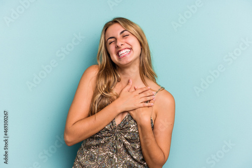 Young caucasian blonde woman isolated on blue background  laughing keeping hands on heart, concept of happiness.