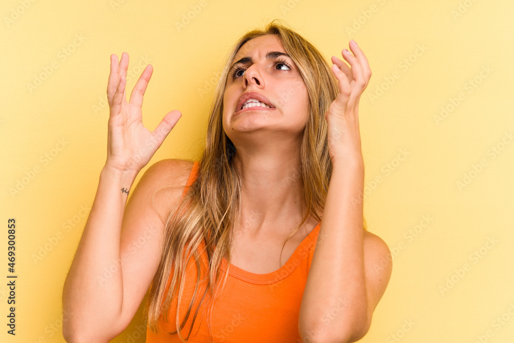 Young caucasian blonde woman isolated on yellow background screaming to the sky, looking up, frustrated. Young caucasian blonde woman isolated on yellow background screaming to the sky, looking up, frustrated.