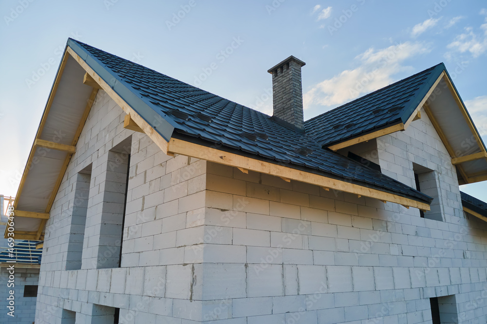 Aerial view of unfinished house with aerated lightweight concrete walls and wooden roof frame covered with metallic tiles under construction Aerial view of unfinished house with aerated lightweight concrete walls and wooden roof frame covered with metallic tiles under construction