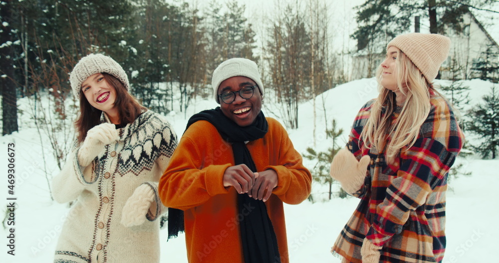 WINTER VACATION. Happy fun multiethnic young friends dance together in warm hats, clothes at snowy forest slow motion.