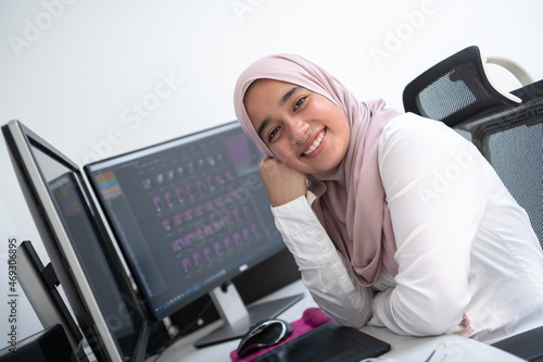 Female Arabic creative professional working at home office on desktop computer with dual screen monitor top view. Selectve focus  photo