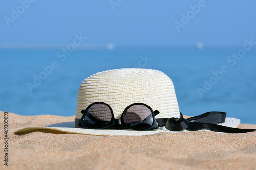 Closeup of yellow straw hat and black protective sunglasses on sandy beach at tropical seaside on warm sunny day. Summer vacation concept
