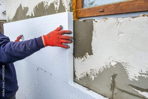 Construction worker installing styrofoam insulation sheets on house facade wall for thermal protection photo