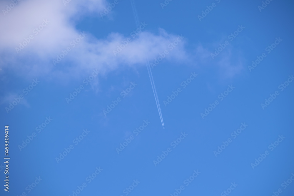 Distant passenger jet plane flying on high altitude on blue sky with white clouds leaving smoke trace of contrail behind. Air traveling concept Distant passenger jet plane flying on high altitude on blue sky with white clouds leaving smoke trace of contrail behind. Air traveling concept