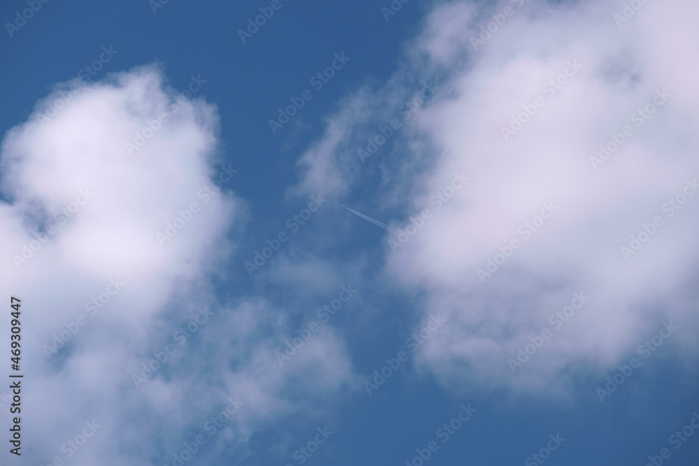 Distant passenger jet plane flying on high altitude on blue sky with white clouds leaving smoke trace of contrail behind. Air traveling concept