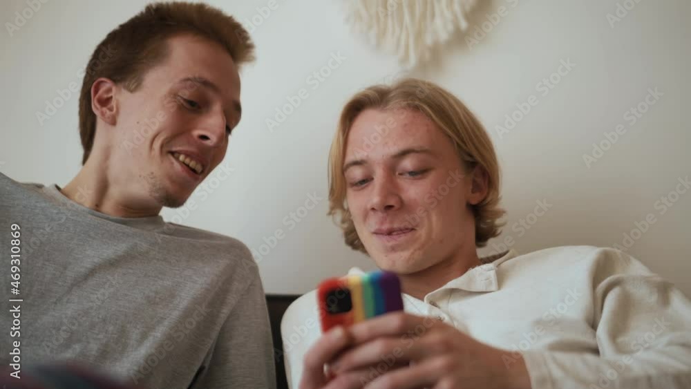 Smiling gay couple looking at the phone and talking on the bed Smiling gay couple looking at the phone and talking on the bed