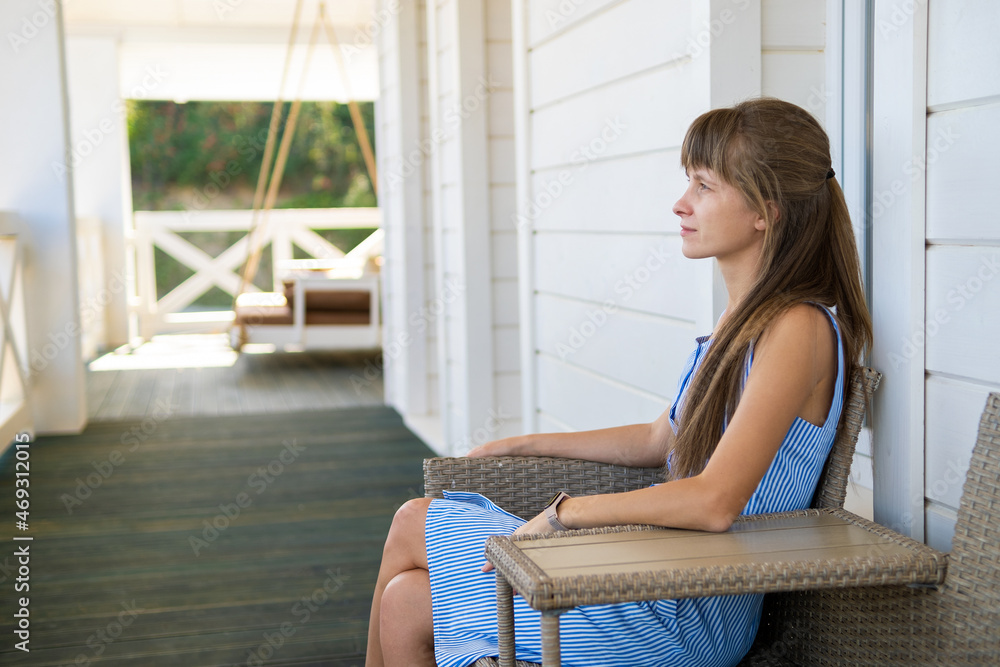 Side view of beautiful brunette woman in blue dress sitting on knitted chair. Concept of relaxing on fresh air on balcony Side view of beautiful brunette woman in blue dress sitting on knitted chair. Concept of relaxing on fresh air on balcony