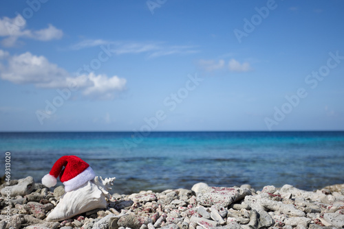 Big seashell with Christmas hat on the coral Caribbean beach. Selective focus.