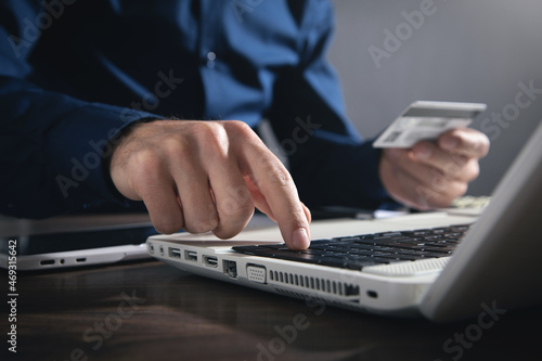 Businessman using laptop computer and holding credit card.