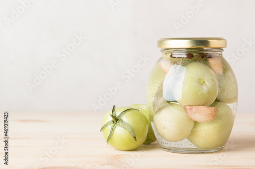 Green tomatoes for canning in a glass jar on a light wooden background. Unripe tomatoes for harvest.