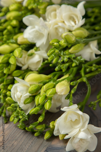 Bouquet of white freesias with lemon-yellow unopened buds on a gray wooden background.