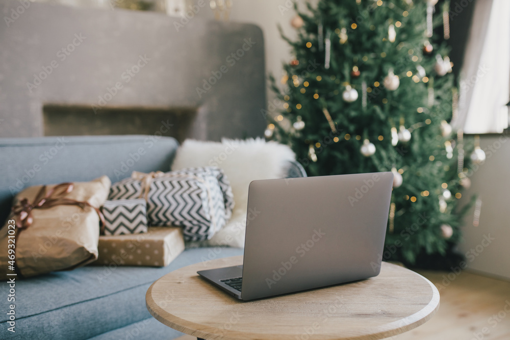 Laptop on table in interior with Christmas tree and presents. Holiday online shopping. Laptop on table in interior with Christmas tree and presents. Holiday online shopping.