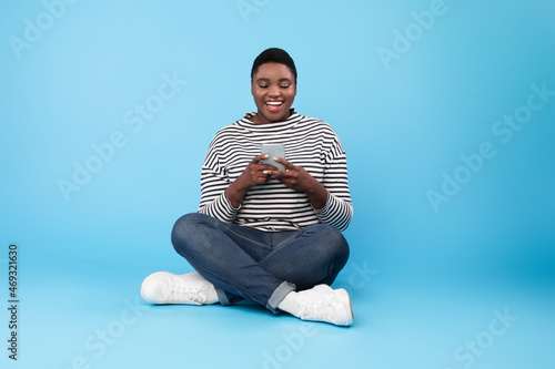Happy Plus Size Black Woman Using Cellpphone Texting Over Blue Background photo
