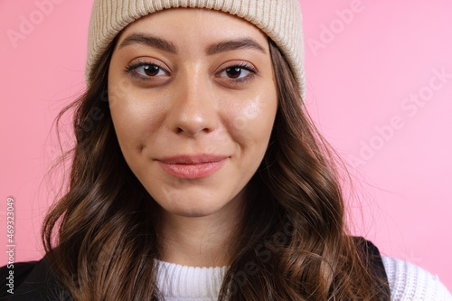 Close-up of young beautiful girl in knitted hat isolated on pink studio background in neon light. Concept of emotions, facial expression