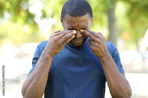 Man with black skin scratching itchy eyes in a park photo